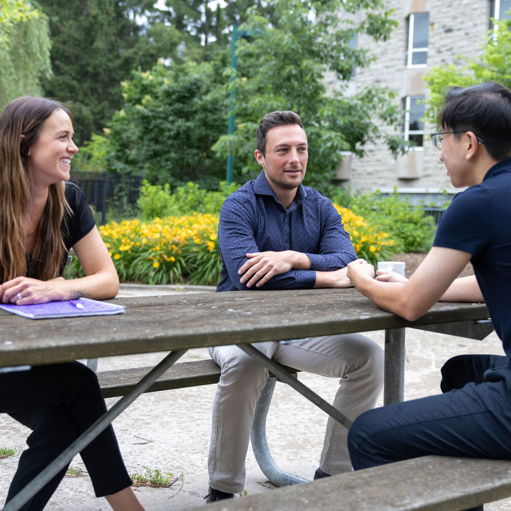 3 people sitting outside at a picnic table talking
